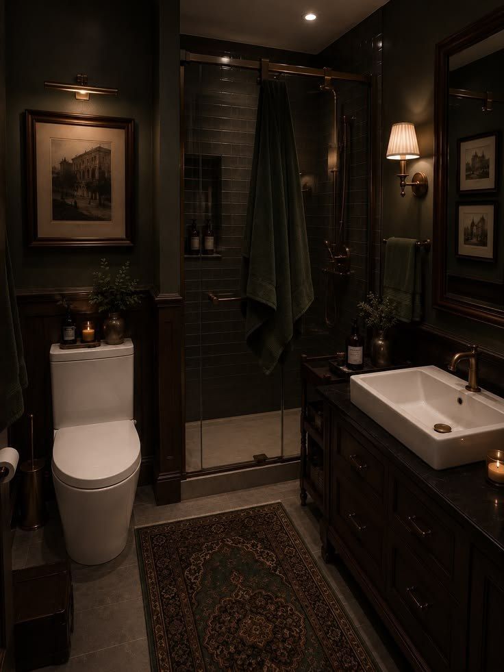 A dark green bathroom with a brass shower bar, a shaded sconce, and one candle.