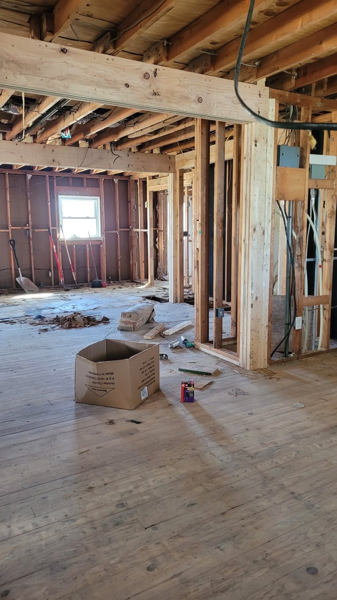 A room opened to the studs, with cable, a window, and the old oak floor still down.
