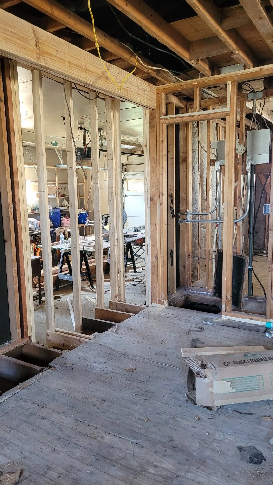 An open wall during construction, with copper supply lines, cable, and the old floor still down.
